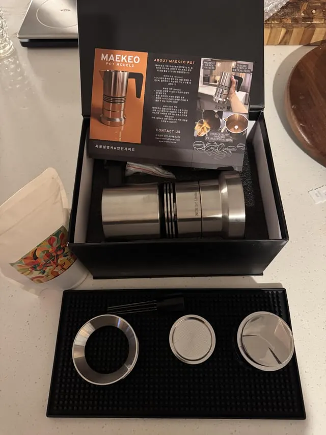 Stainless steel Maekeo moka pot in its box with the separate parts laid out on a bar mat