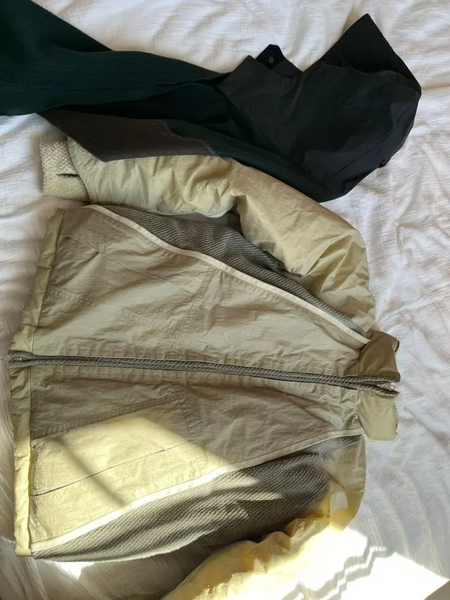 Beige and black zip-up jackets laid out on a bed