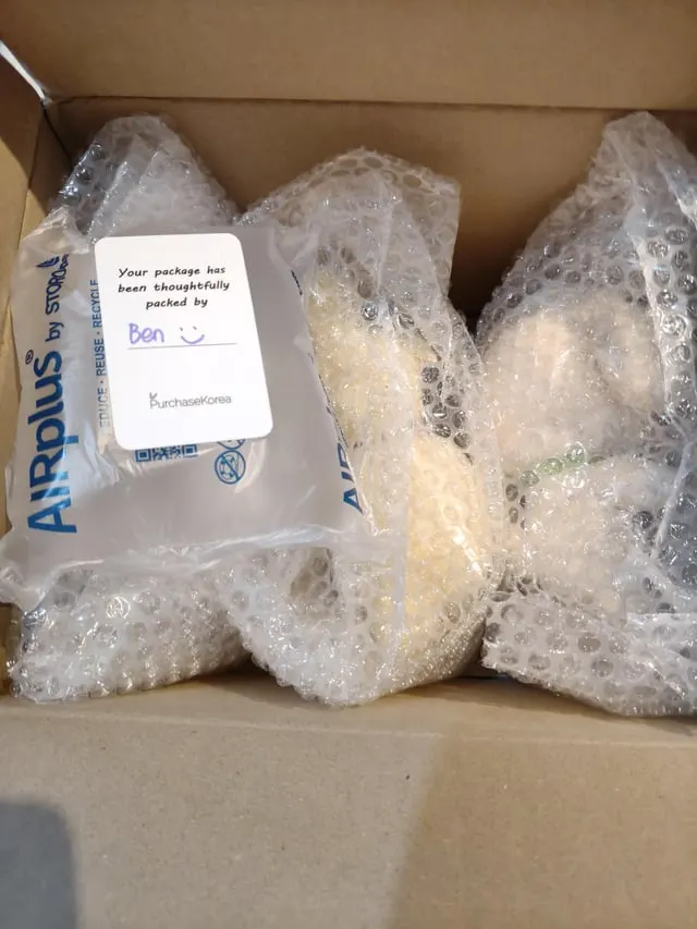 Bubble-wrapped items in a shipping box with a handwritten PurchaseKorea packing card